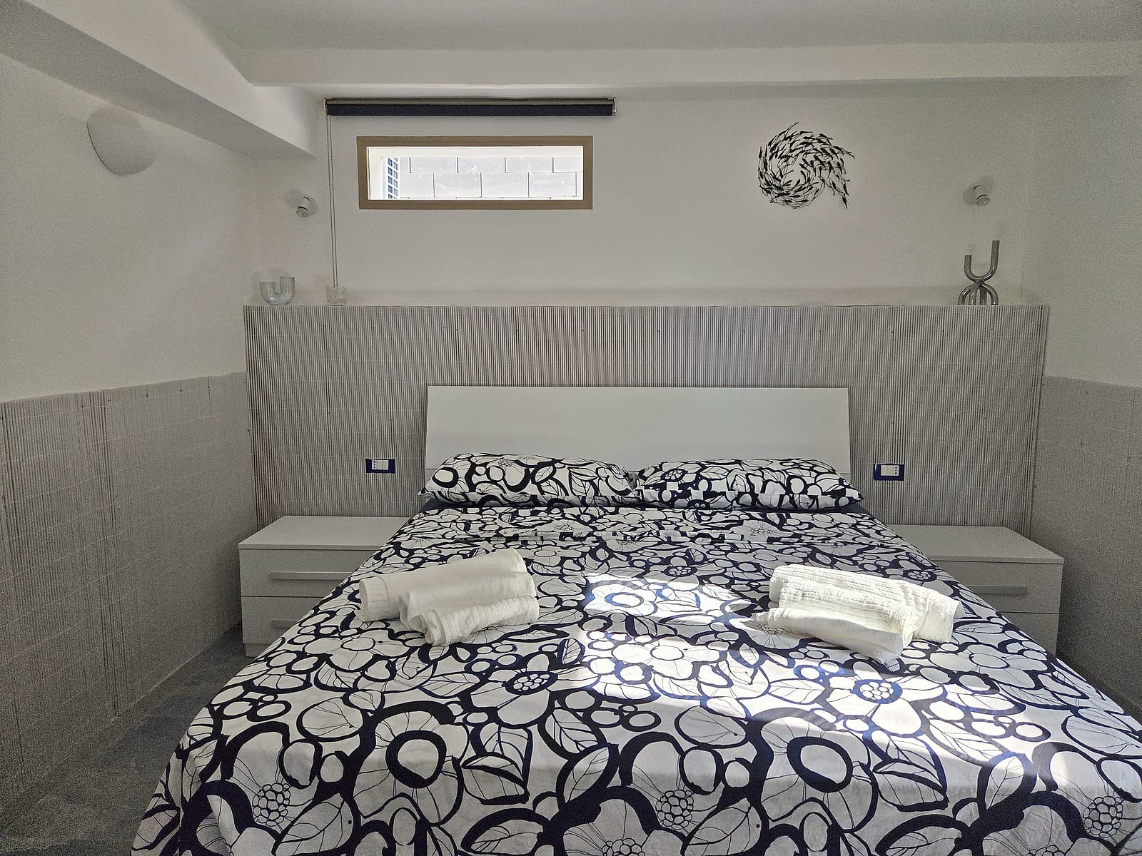 Camera matrimoniale con copriletto a fiori bianco e blu, comodini e asciugamani pronti