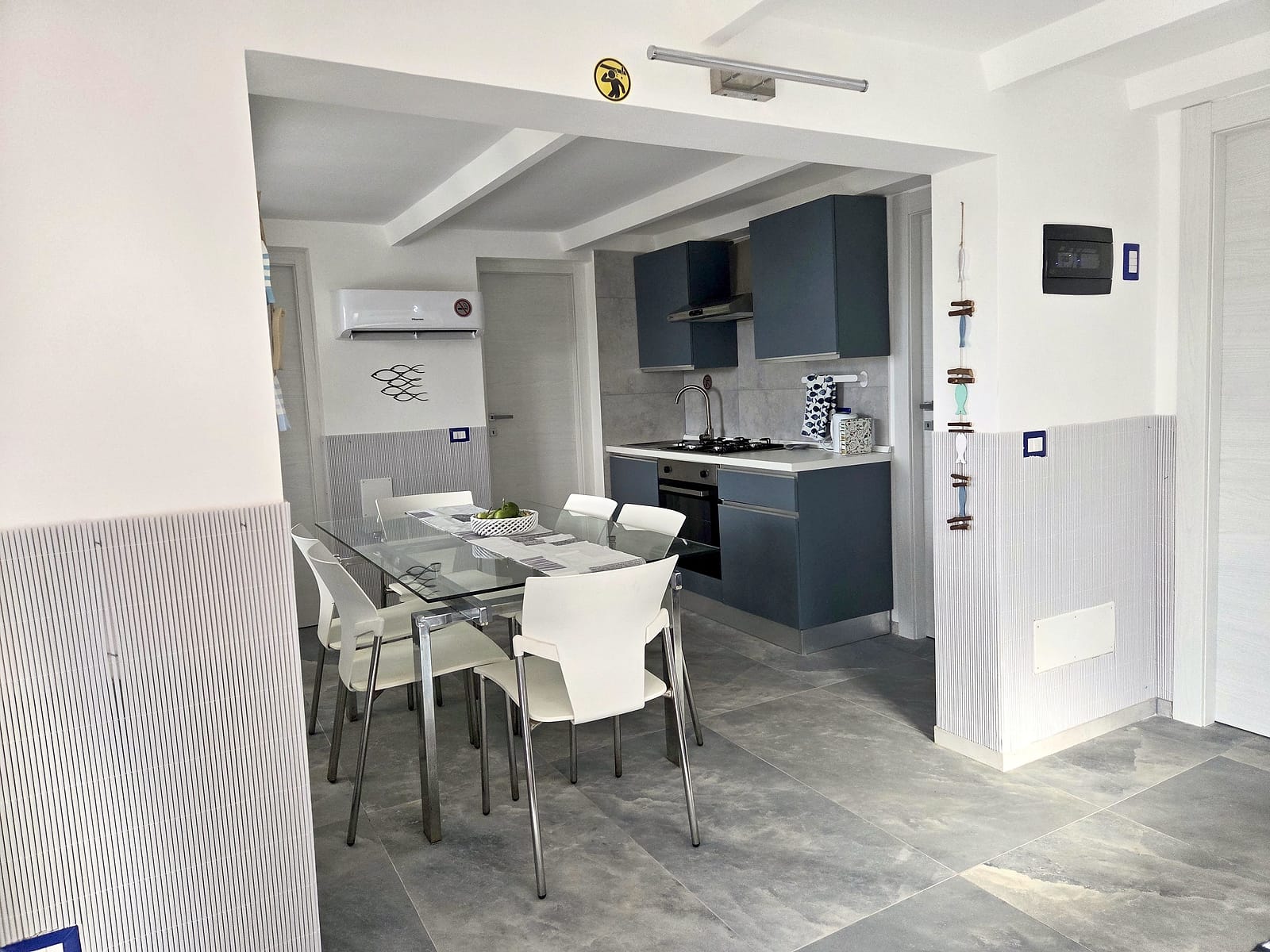Cucina blu e zona pranzo con tavolo in vetro e sedie bianche, viste attraverso l'arco