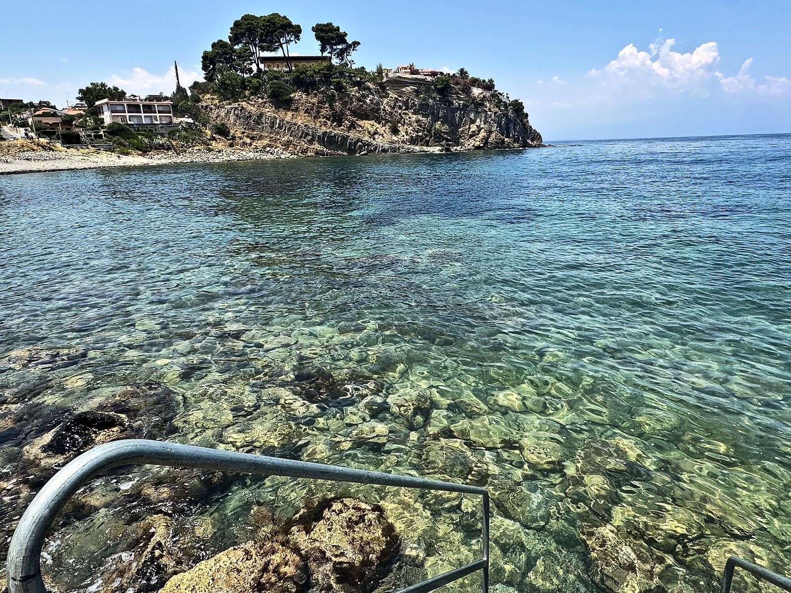 Crystal-clear water among the rocks of the bay, with a ladder into the sea