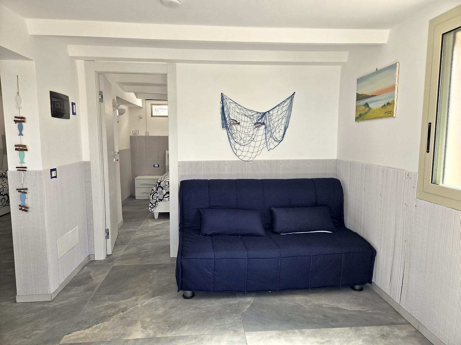 Soggiorno con divano letto blu, rete da pesca decorativa e quadro di mare