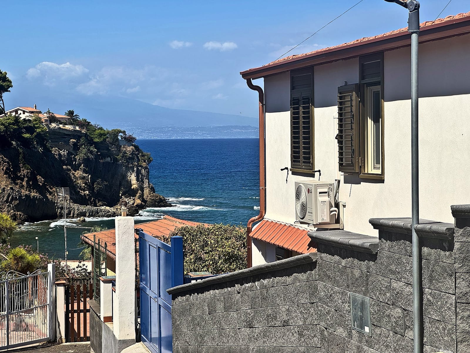 The Etna Lemon Sea villa with its blue gate, the cliffs, the sea and Etna on the horizon